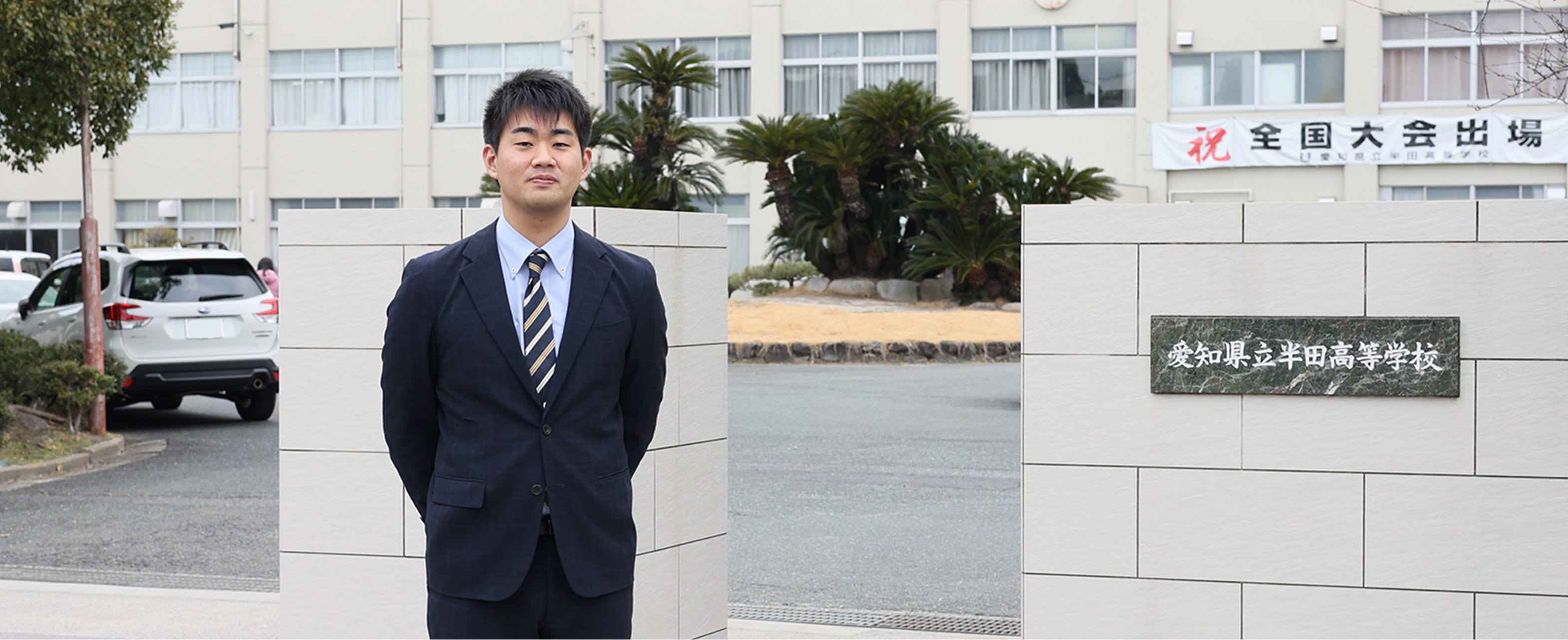 愛知県立半田高等学校の玄関前に立ち後ろで手を組む男性